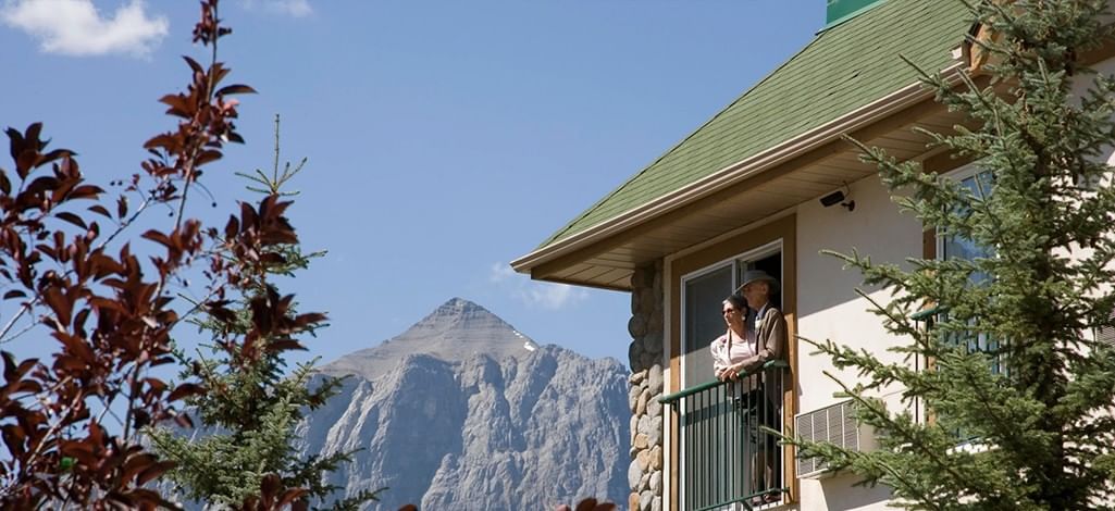 A couple enjoying the balcony at a Canmore hotel close to Main Street and mountains behind.