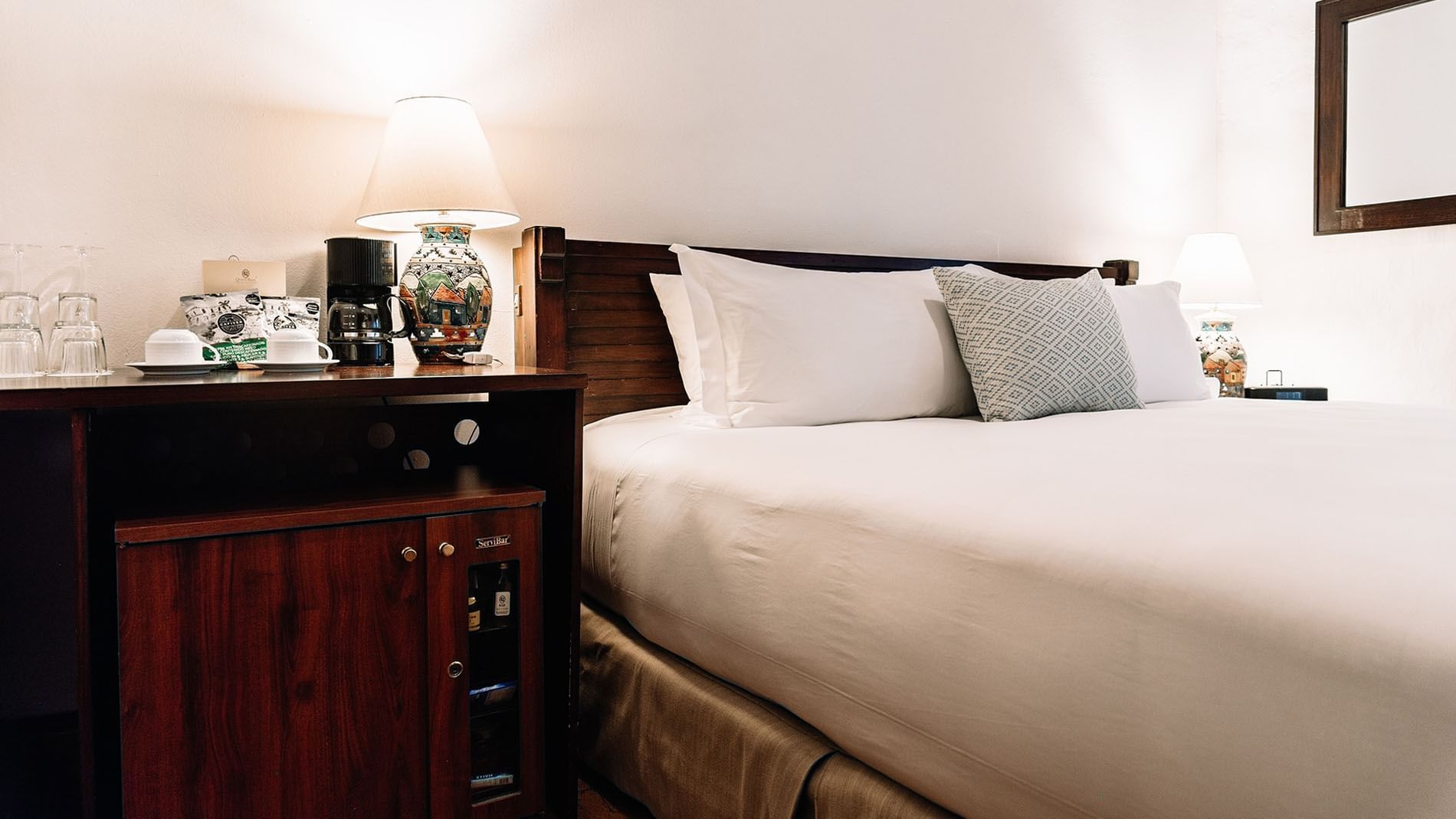 Side cupboard and coffee maker by the cozy bed with plush pillows in the King Novicia Suite at Quinta Real Oaxaca