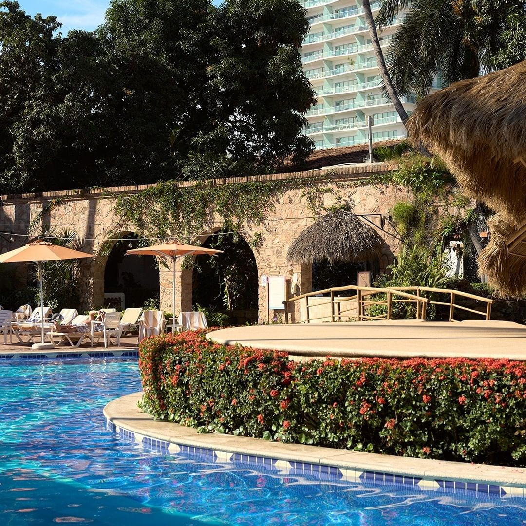 Swimming pool with lounge chairs and umbrellas under a blue sky.
