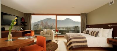 Mesa de comedor y escritorio junto a la cama con vista a la montaña desde la ventana en Terrace Suite de NOI Vitacura