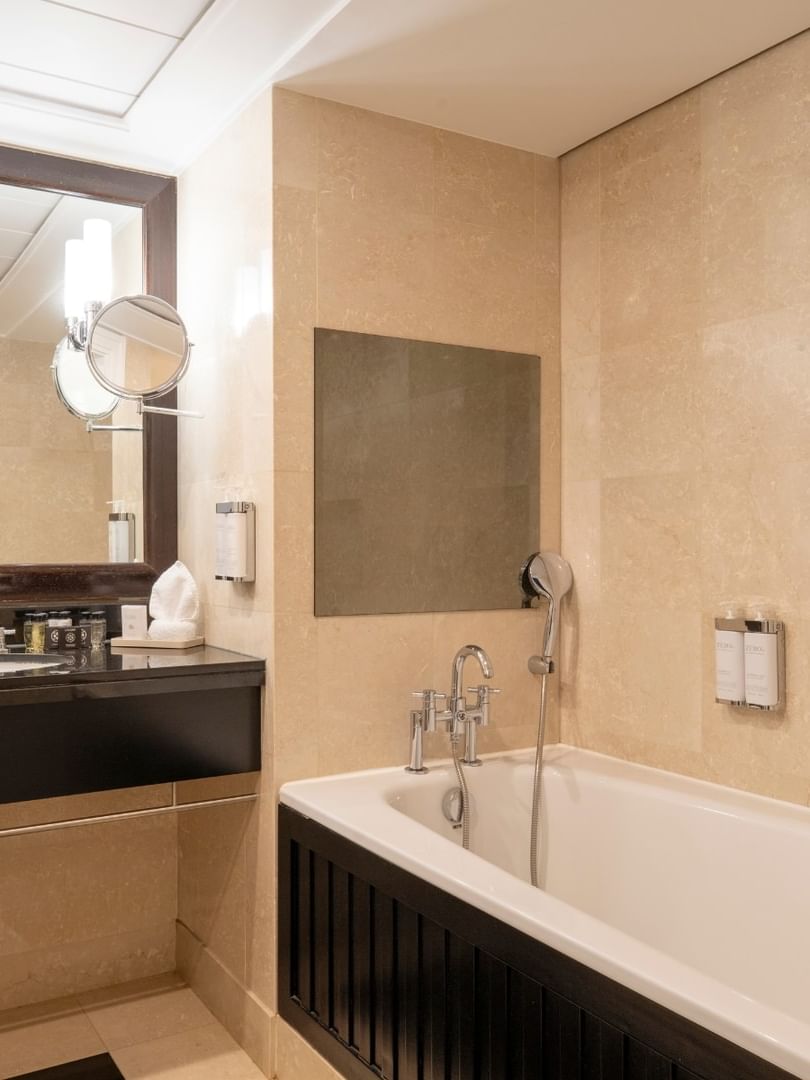 White bathtub by a black vanity under a large dark-framed mirror in The Champs-Élysées Suite at Warwick Paris Champs Elysées