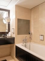 White bathtub by a black vanity under a large dark-framed mirror in The Champs-Élysées Suite at Warwick Paris Champs Elysées
