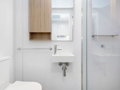 White bathroom with toilet, sink, mirror, and glass shower enclosure.
