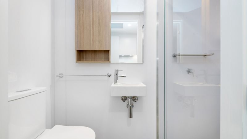 White bathroom with toilet, sink, mirror, and glass shower enclosure.