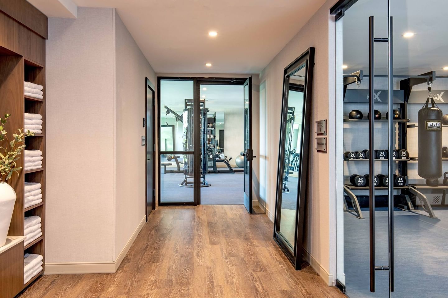 A hallway with open doors leading to a gym with exercise equipment and mirrors on the walls.