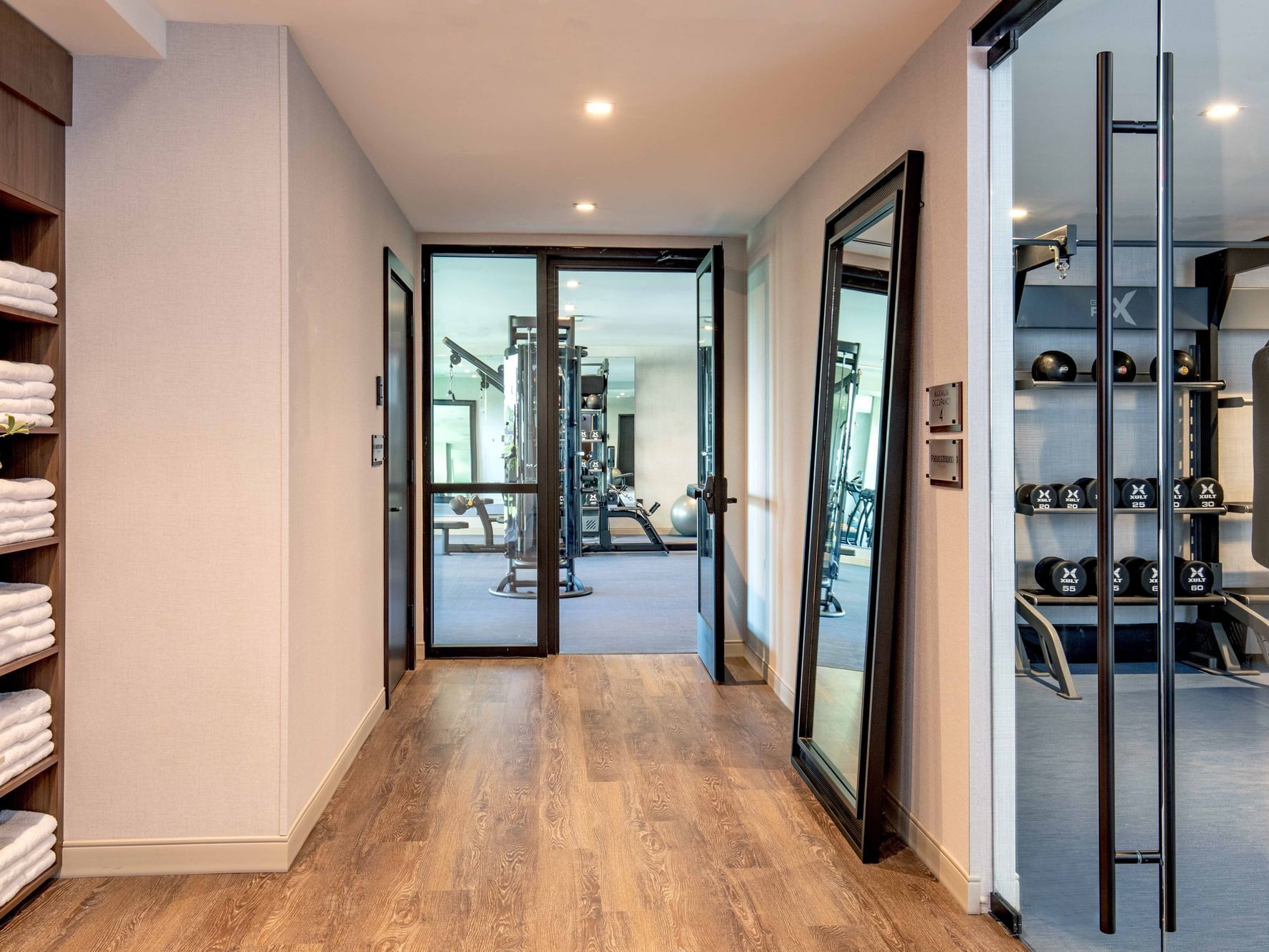 Hallway with wooden floors, towels, and mirrors leading to a gym with equipment and a punching bag.