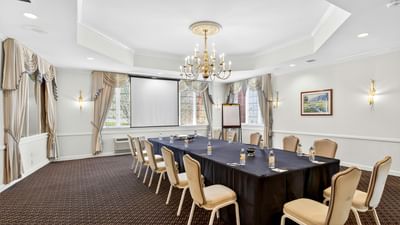 Boardroom setup with a long table surrounded by chairs under a crystal chandelier in the Talcott Room at Avon Old Farms Hotel