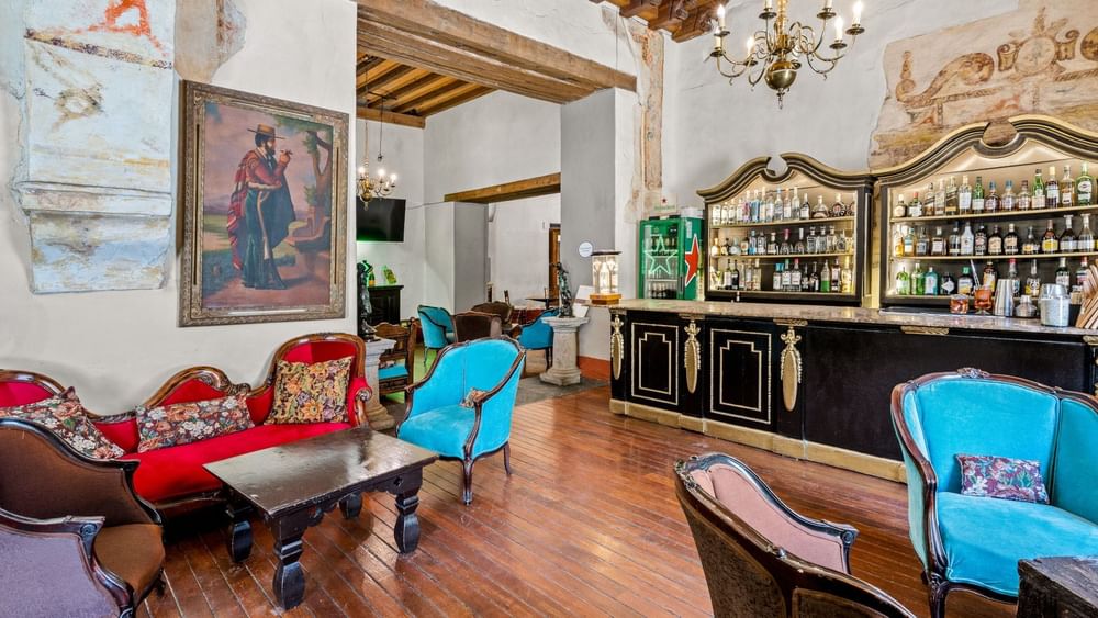 A lounge with a bar, wooden floor, and various furniture at Quinta Real Puebla
