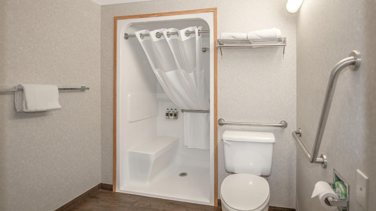 An accessible bathroom with a toilet, shower stall, towel racks, and safety bars.