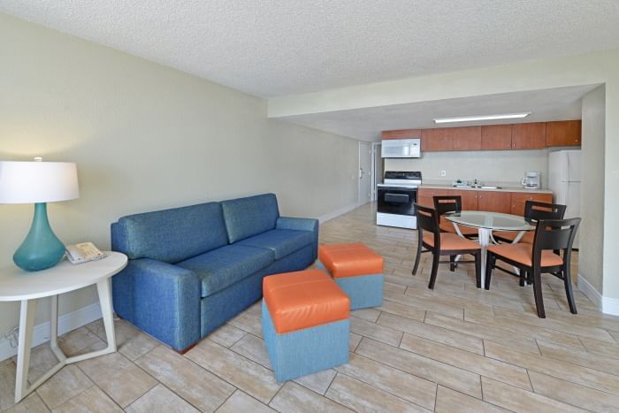 A wide view of a suite's living area with a kitchenette, dining table, sofa, and stools.