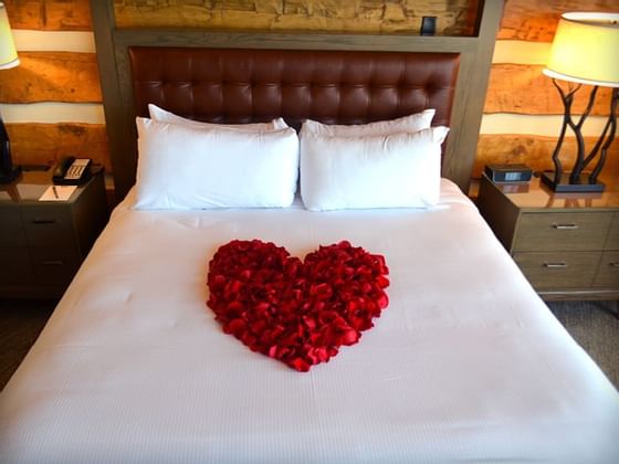 Queen bed with rose petals arranged in the form of a heart on it