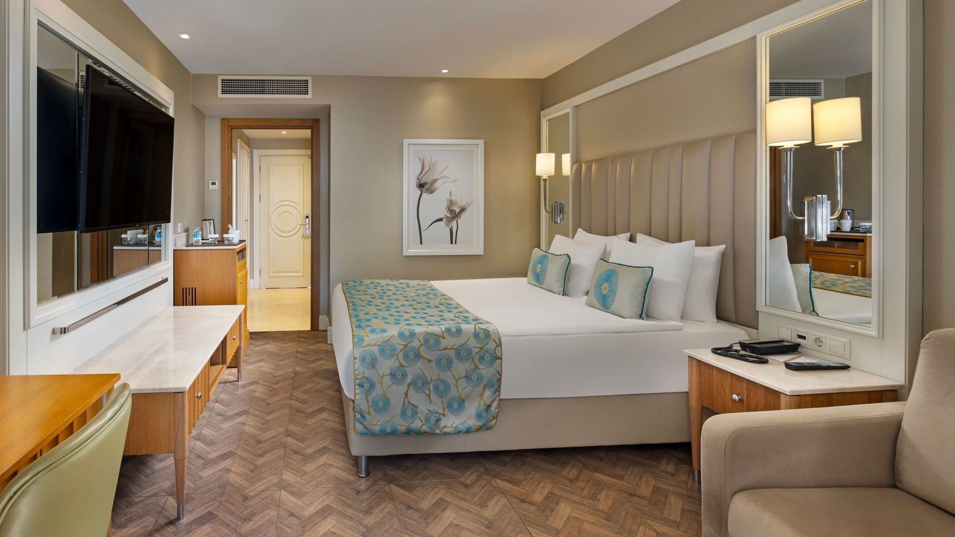 Titanic Deluxe Lara – Annex Standard Pool’da yatak, masa ve büyük aynalı şık bir lüks oda.