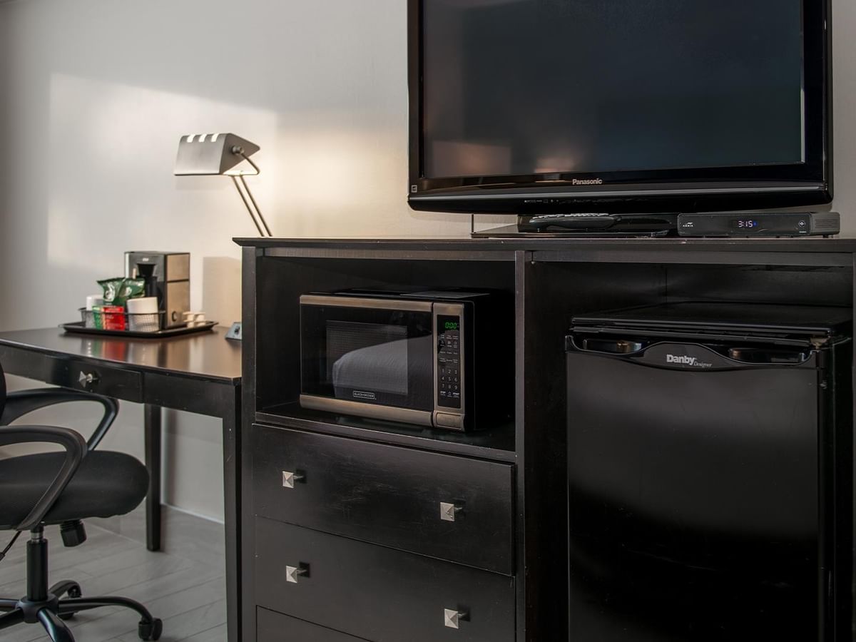 Desk with chair, TV, microwave, and mini fridge in a hotel room.