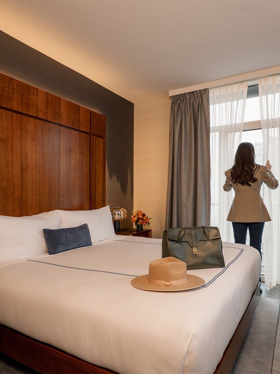 Gansevoort Suite with wood-paneled headboard, white bedding, and guest at window at Gansevoort Meatpacking NYC - NEW