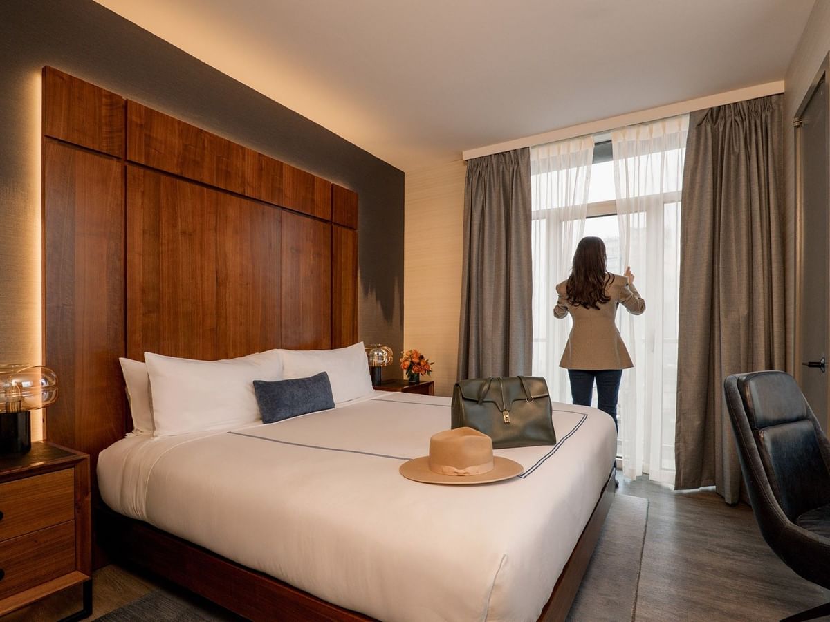 Gansevoort Suite with wood-paneled headboard, white bedding, and guest at window at Gansevoort Meatpacking NYC - NEW