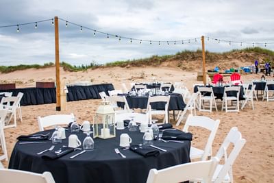 Round dining tables set up on the sand for outdoor events in Prince Edward Island at Rodd Crowbush Golf & Beach Resort