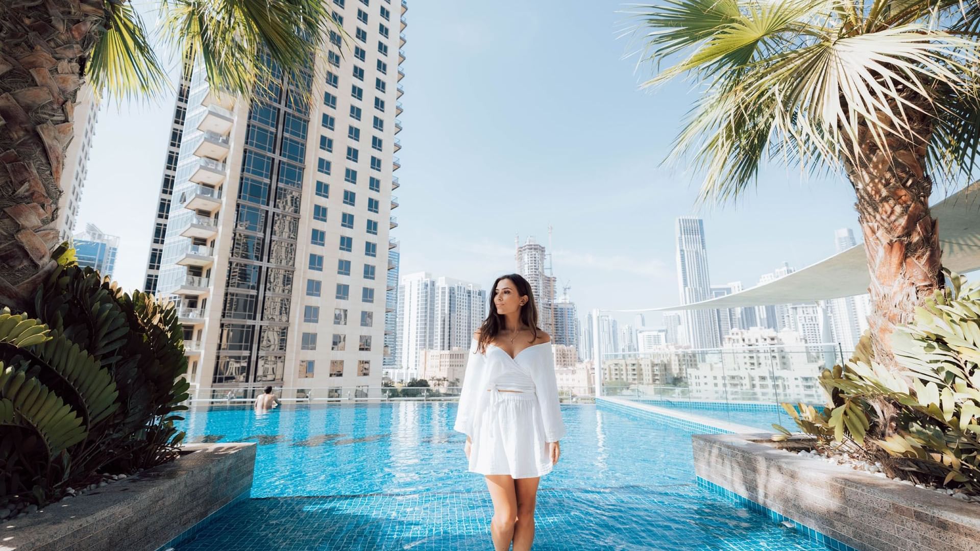 A woman in a white dress standing in a hotel pool at DAMAC Maison Distinction