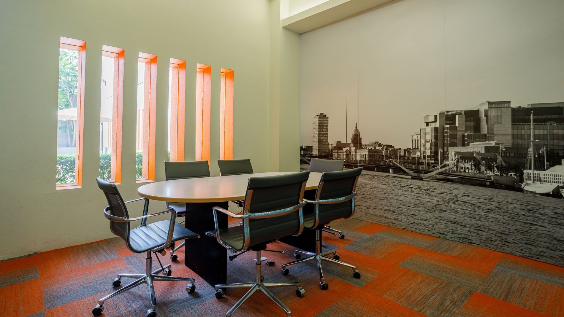Small meeting space at Real Inn Torreon, with an oval table, black rolling chairs, and orange window accents