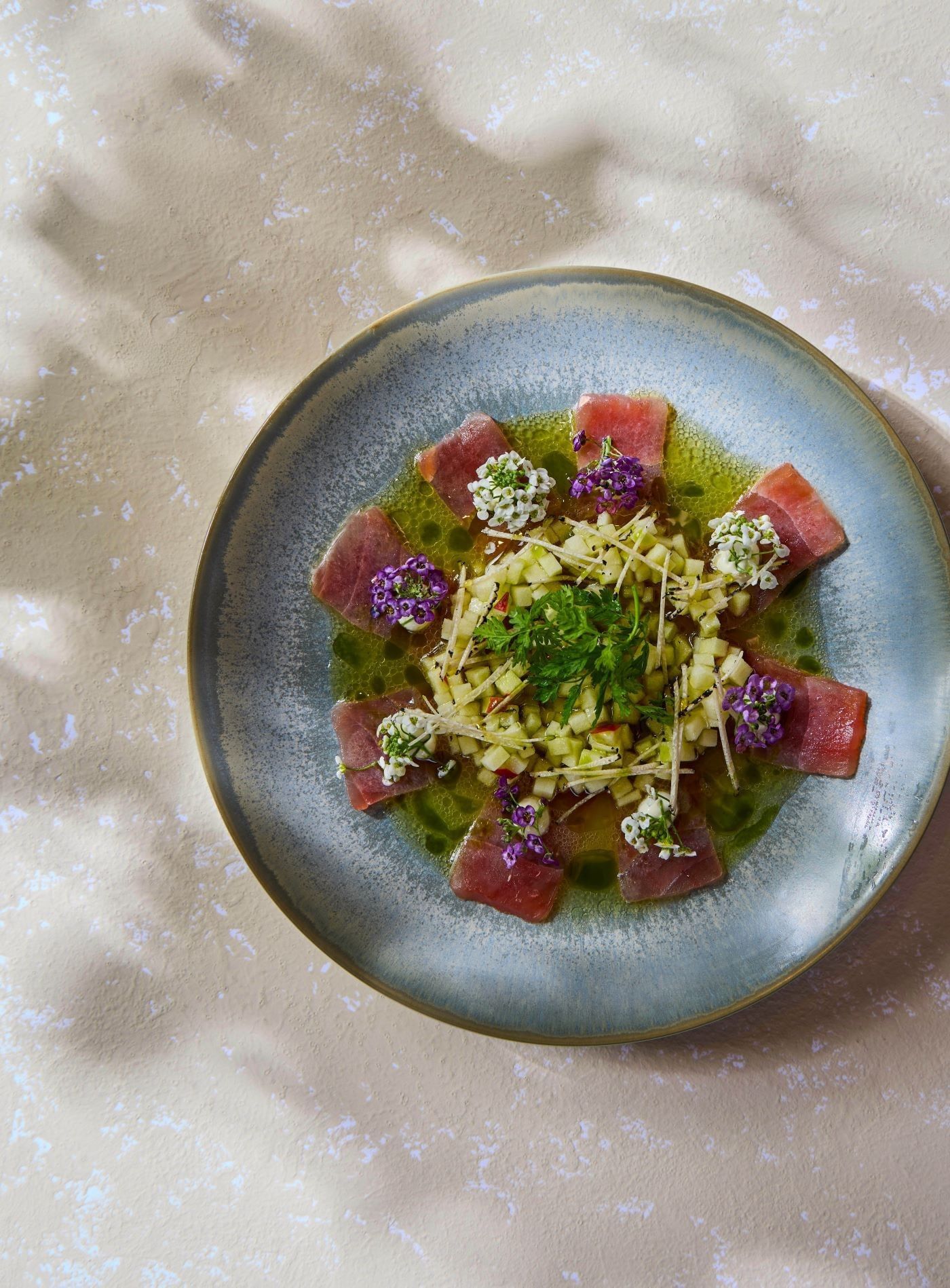 Tuna carpaccio with flowers on a blue plate from the à la carte menu at Whitcomb\'s inside The Londoner Hotel