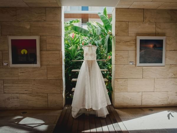 White lacy wedding dress hanging in an archway with lush green plants in the backdrop at The Explorean Resorts