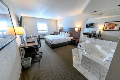 TV & work desk facing king bed with open bathtub in Spa Suite at Service Plus Inns & Suites