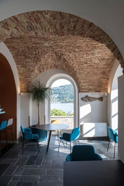 Salon intérieur avec voûte en brique, meubles bleus, vue sur la mer et poisson mural.