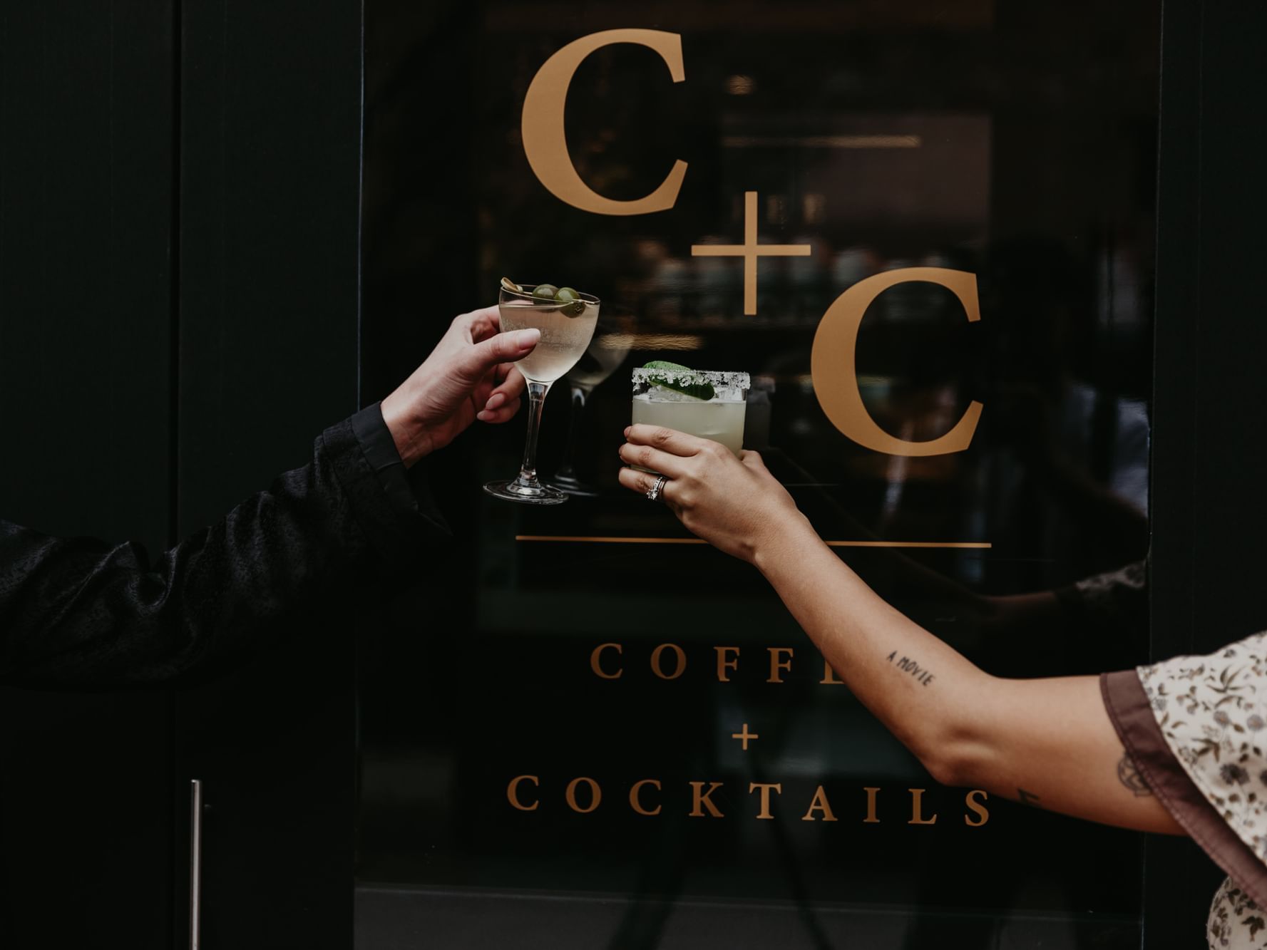Two people holding cocktails in front of restaurant sign
