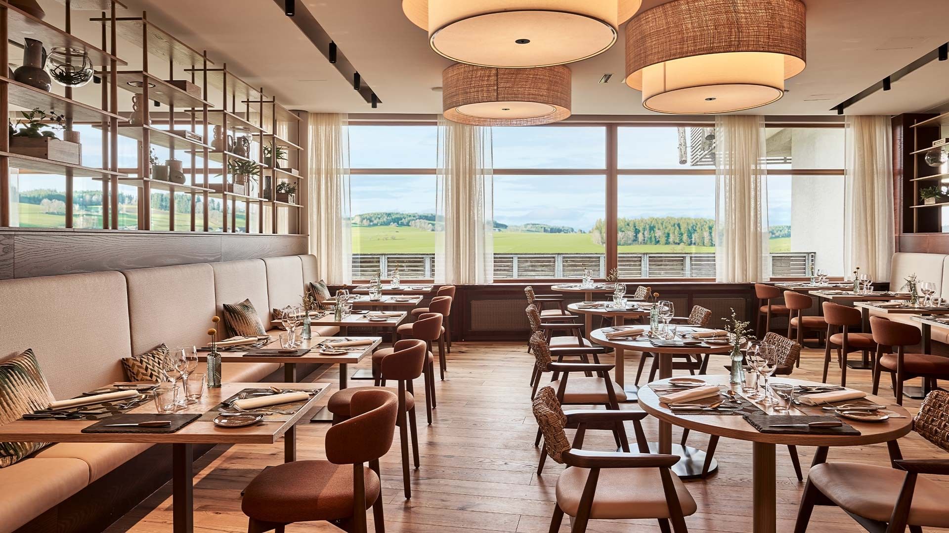 Ein modernes Restaurant mit Holztischen und Stühlen und Blick auf eine grüne Wiese bei Falkensteiner Hotel
