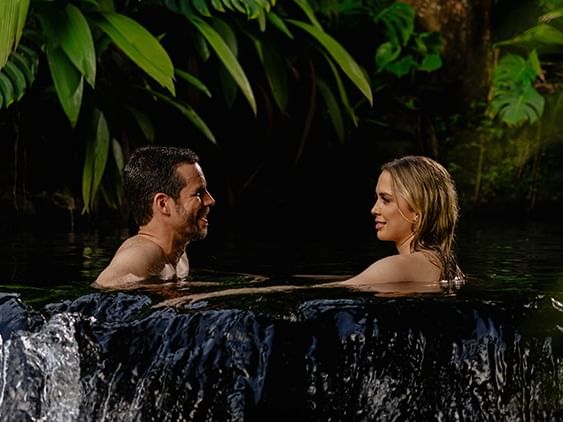 Pareja relajándose en piscina de borde infinito rodeada de vegetación tropical exuberante