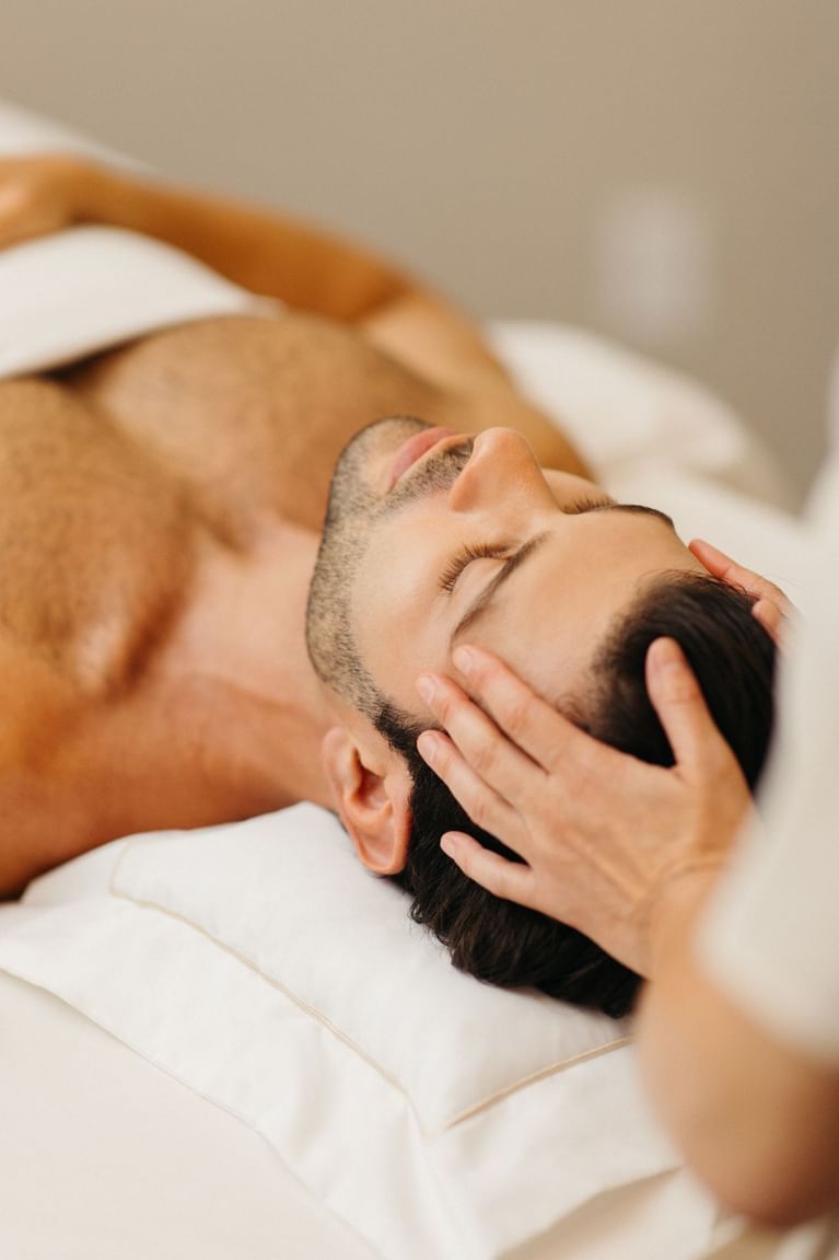 Close-up of man relaxing on spa table with eyes closed receiving head and forehead massage treatment at Hotel X Toronto