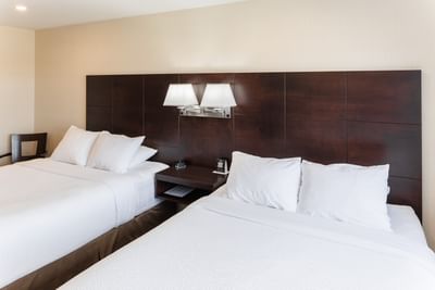 Close-up of two beds with white linens divided by wood nightstand and silver lamps in Royalty Two Doubles at Rodd Royalty