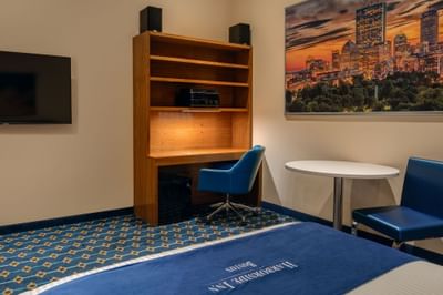 Shelf unit with a desk underneath and a table with chairs near skyline art in Double Queen Atrium at Harborside Inn Boston