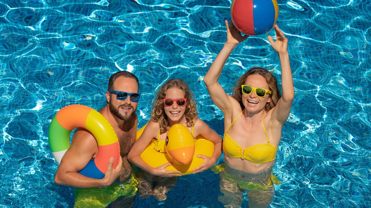 Three people wearing sunglasses and holding inflatables in a pool for the Splish, Splash & Save offer.
