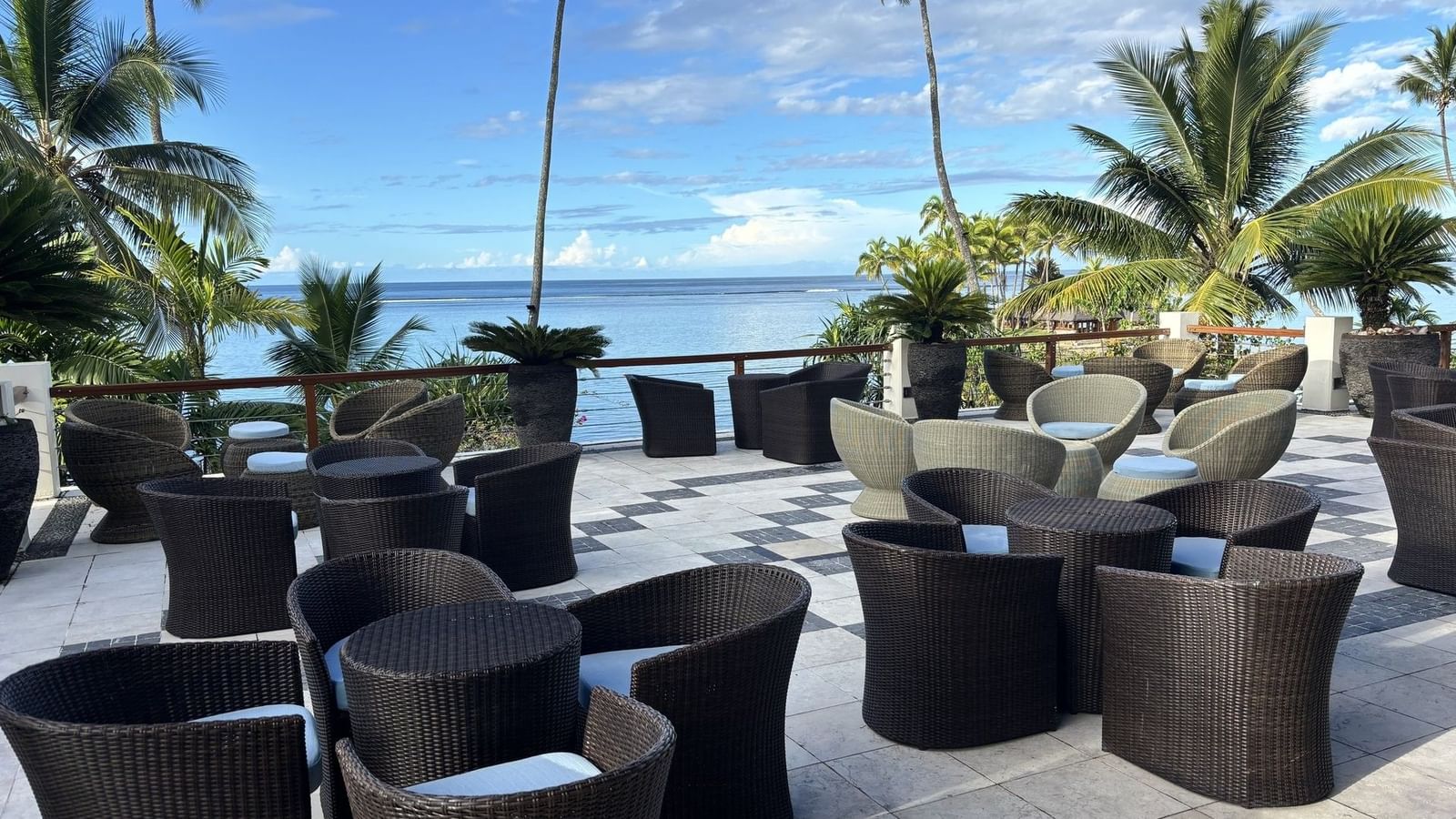 Woven chairs by a stone railing under palm trees in Sunset Terrace Bar at Warwick Fiji Resort and Spa