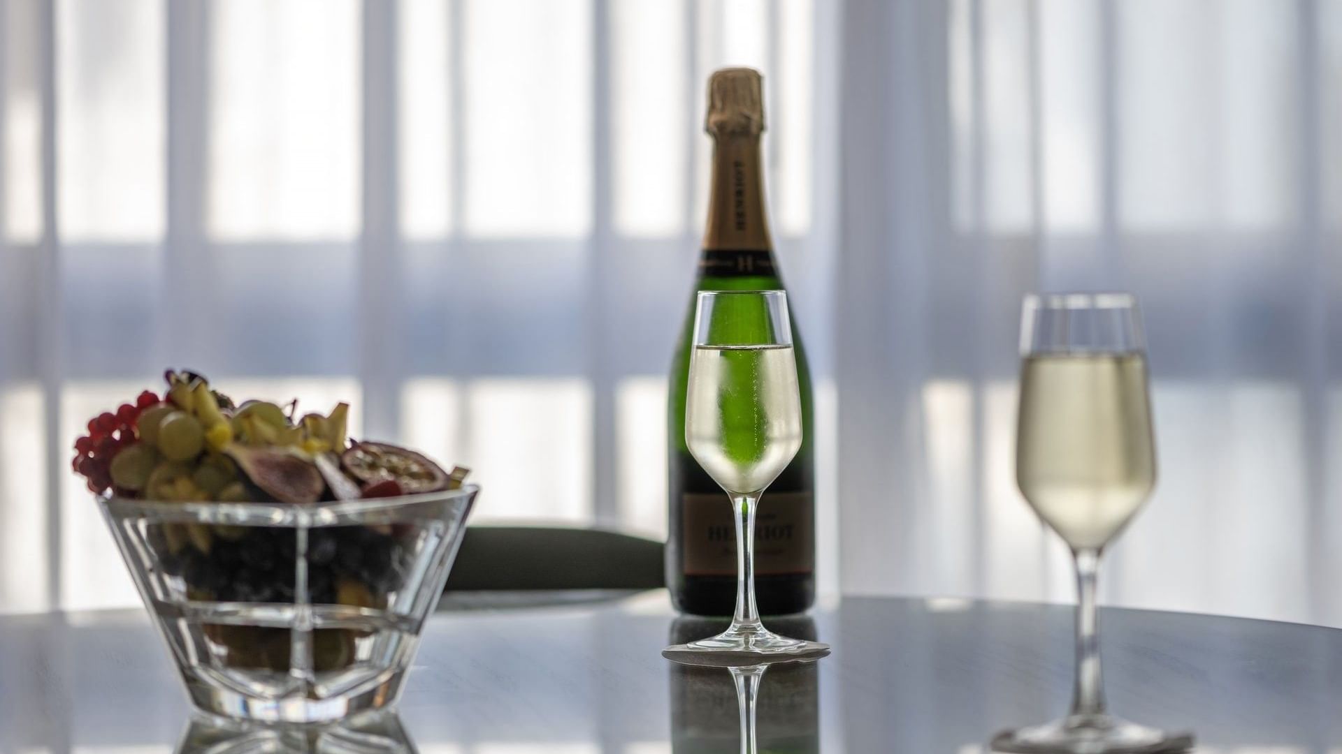 Glass of wine and a bottle on a reflective table with soft light filtering through curtains at Warwick Reine Astrid - Lyon