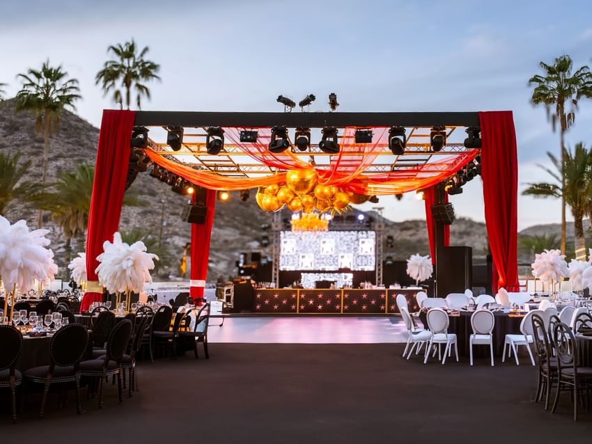 New year's eve vintage circus setup with a stage red drapes and dining tables under palm trees at Marquis Los Cabos Resort