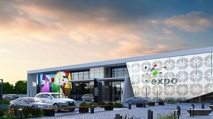 Dhahran Expo by parked cars under a soft sunset sky with vibrant banners near Naviti by Warwick Al Khobar