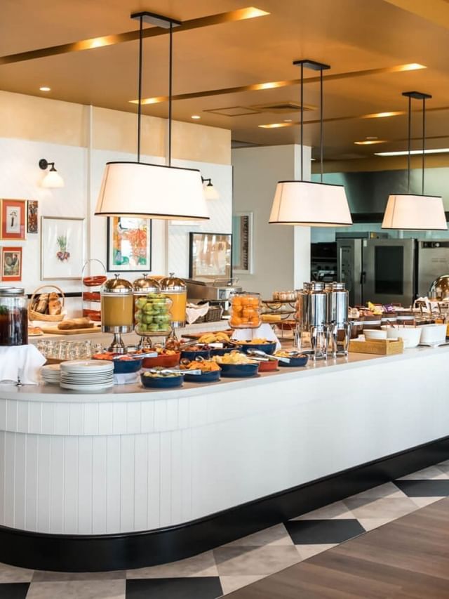 Breakfast at Elysium Manly with a long counter by juices under pendant lamps surrounding a black-and-white tiled floor