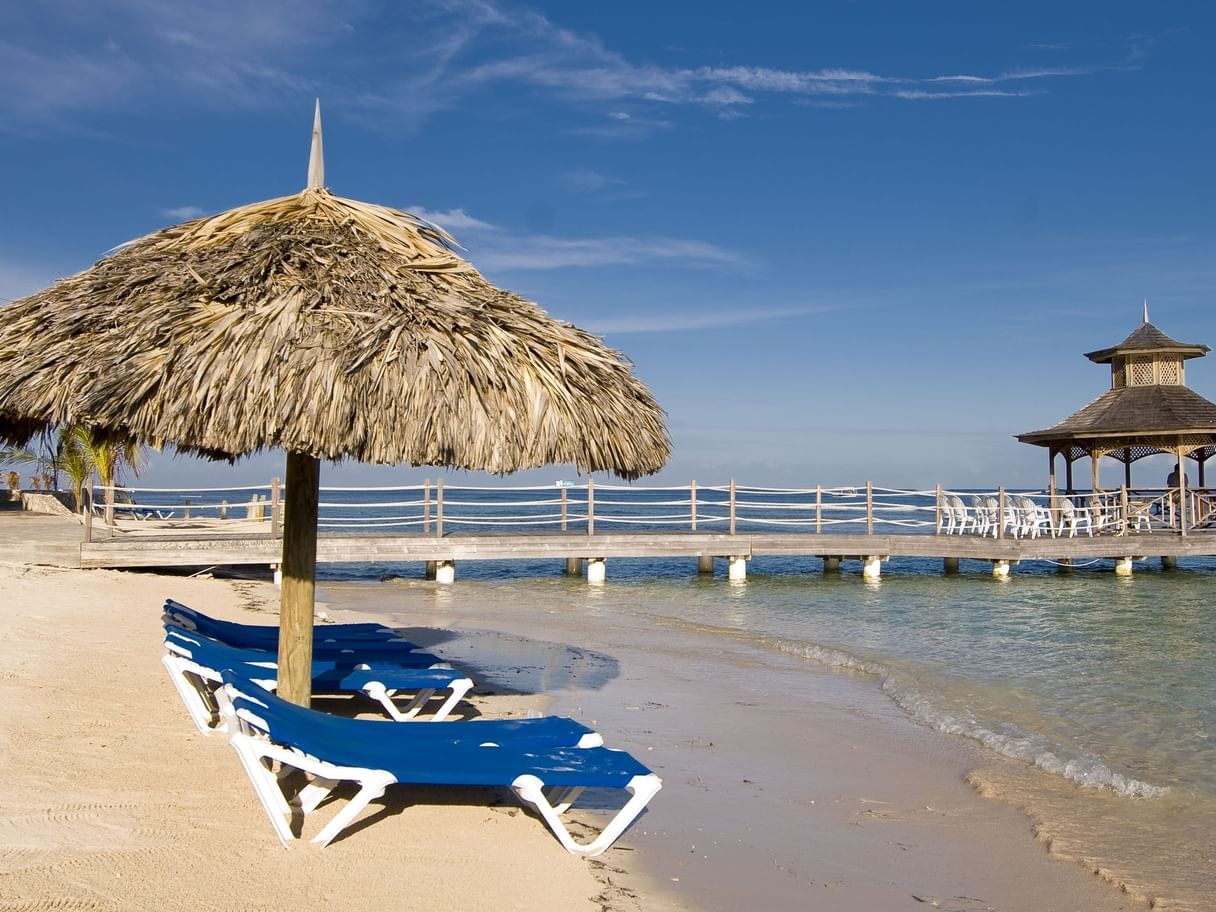 Landscape view of a straw beach umbrella & sunbeds by the sea on a sunny day at Holiday Inn Montego Bay