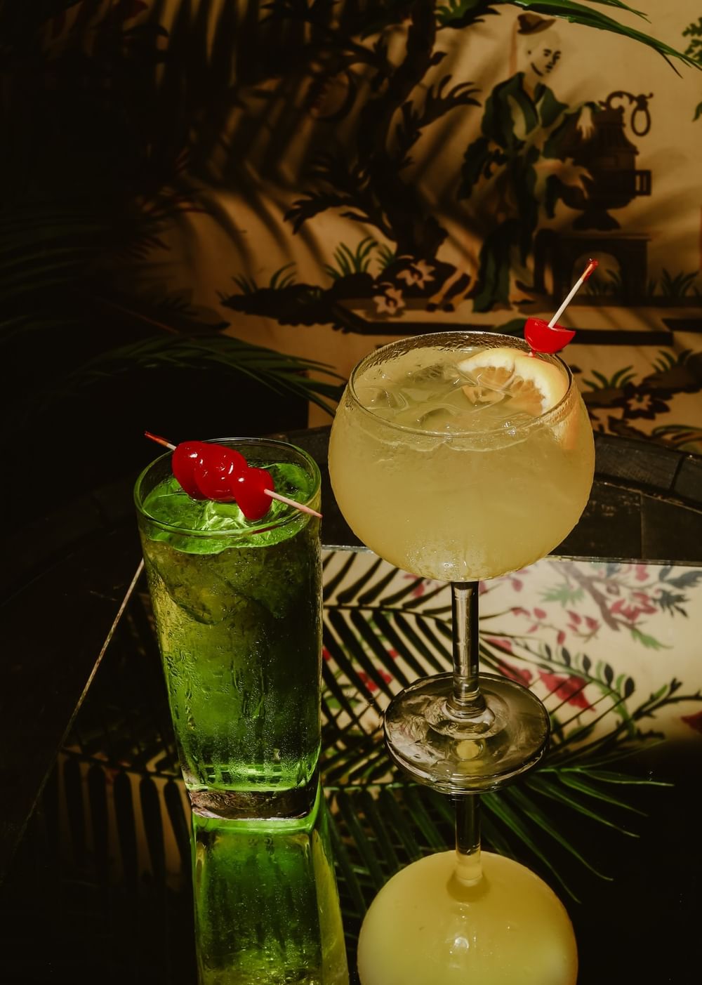 Two chilled cocktails with cherries on a glass table by tropical wall art at Arlington Resort Hotel & Spa