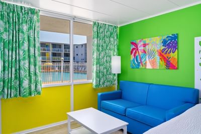 Upper Floor Streetview Efficiency room with sofa, green walls, leafy curtains & pool view through window at Kokomo Suites