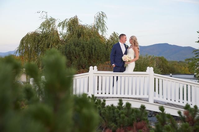 Bride and groom standing close on a white footbridge, near mountains and pines at Mountain View Grand Resort & Spa