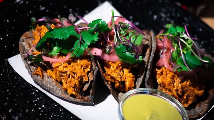 Close-up of three artisanal tacos filled with meat and garnished with herbs and onions at Media Sangre in Araiza Calafia