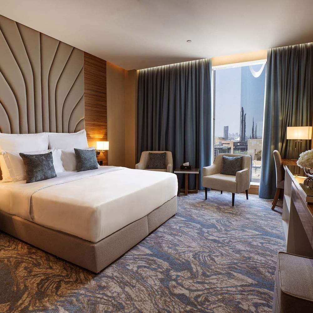 King bed with a tall fluted headboard by a window under blue drapes in Royal Suite at Cantonal Hotel by Warwick Riyadh