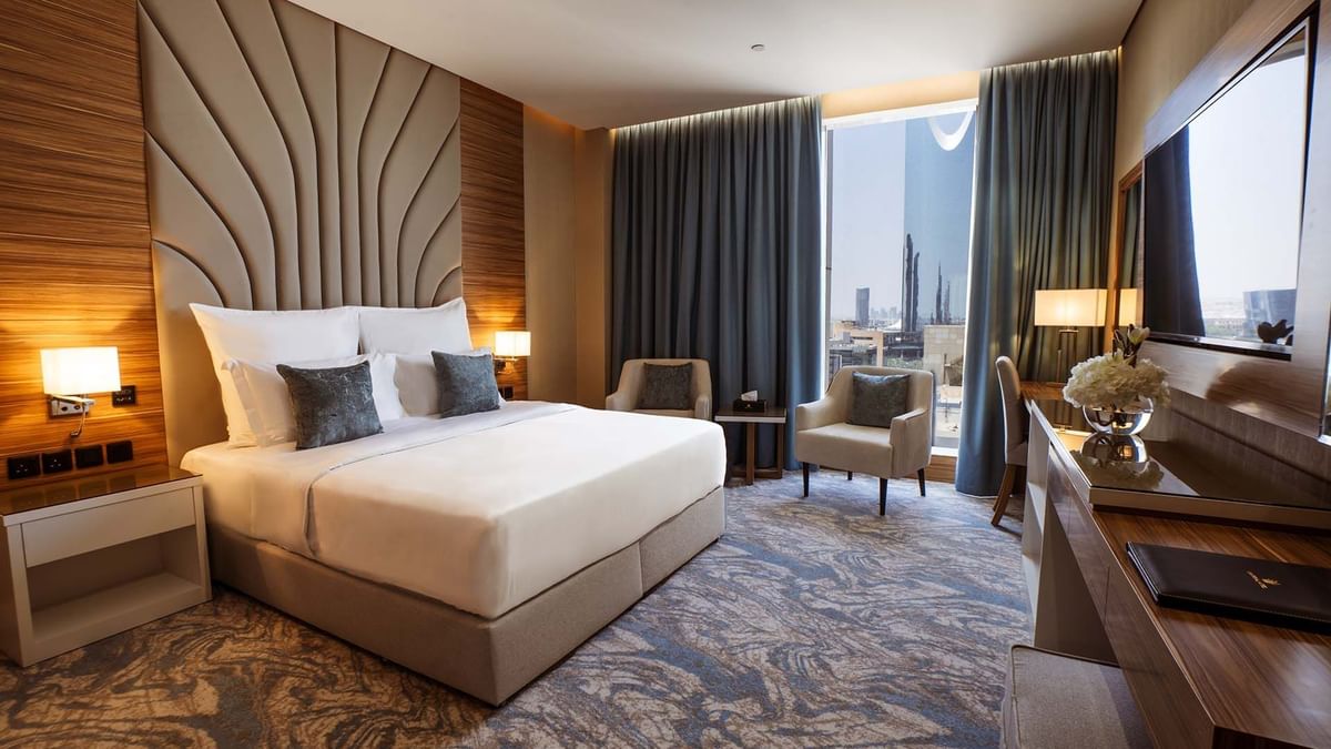 King bed with a tall fluted headboard by a window under blue drapes in Royal Suite at Cantonal Hotel by Warwick Riyadh