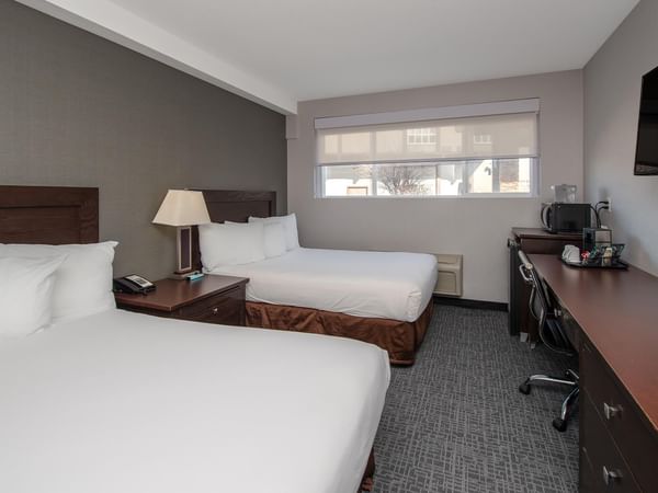 Two beds with pillows and a desk with a TV in a room.