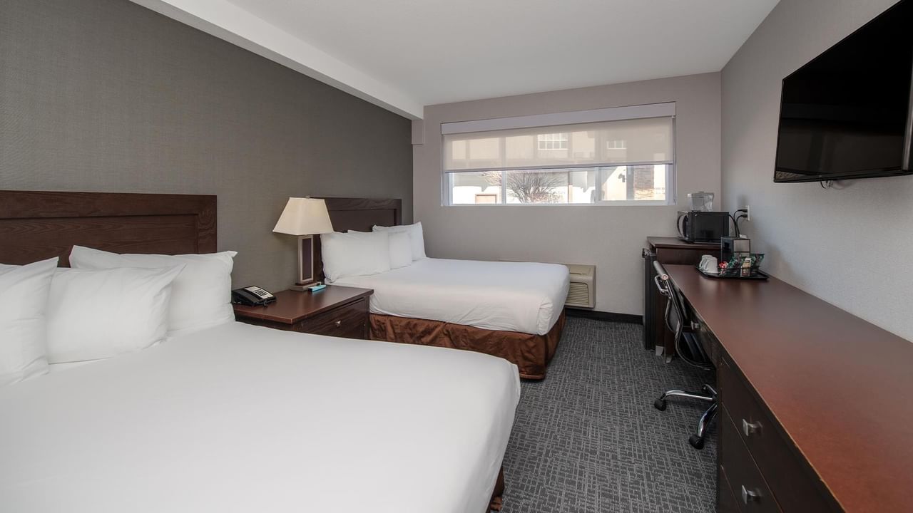 Two beds with pillows and a desk with a TV in a room.
