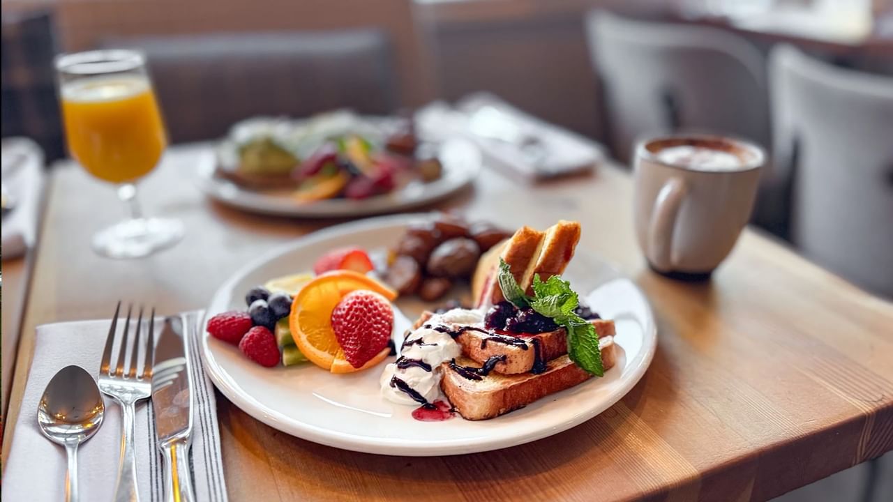 Plates of french toast and avocado toast on a restaurant table, along with coffee and orange juice.