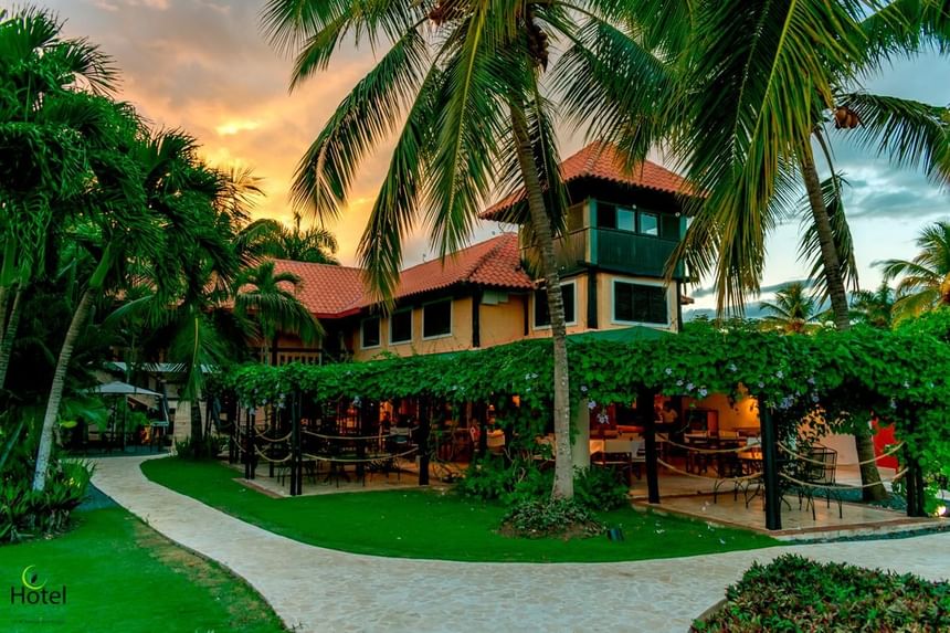 Garden Restaurant with a red-tiled roof surrounded by lush palm trees and greenery at Hotel La Casita by The Hub