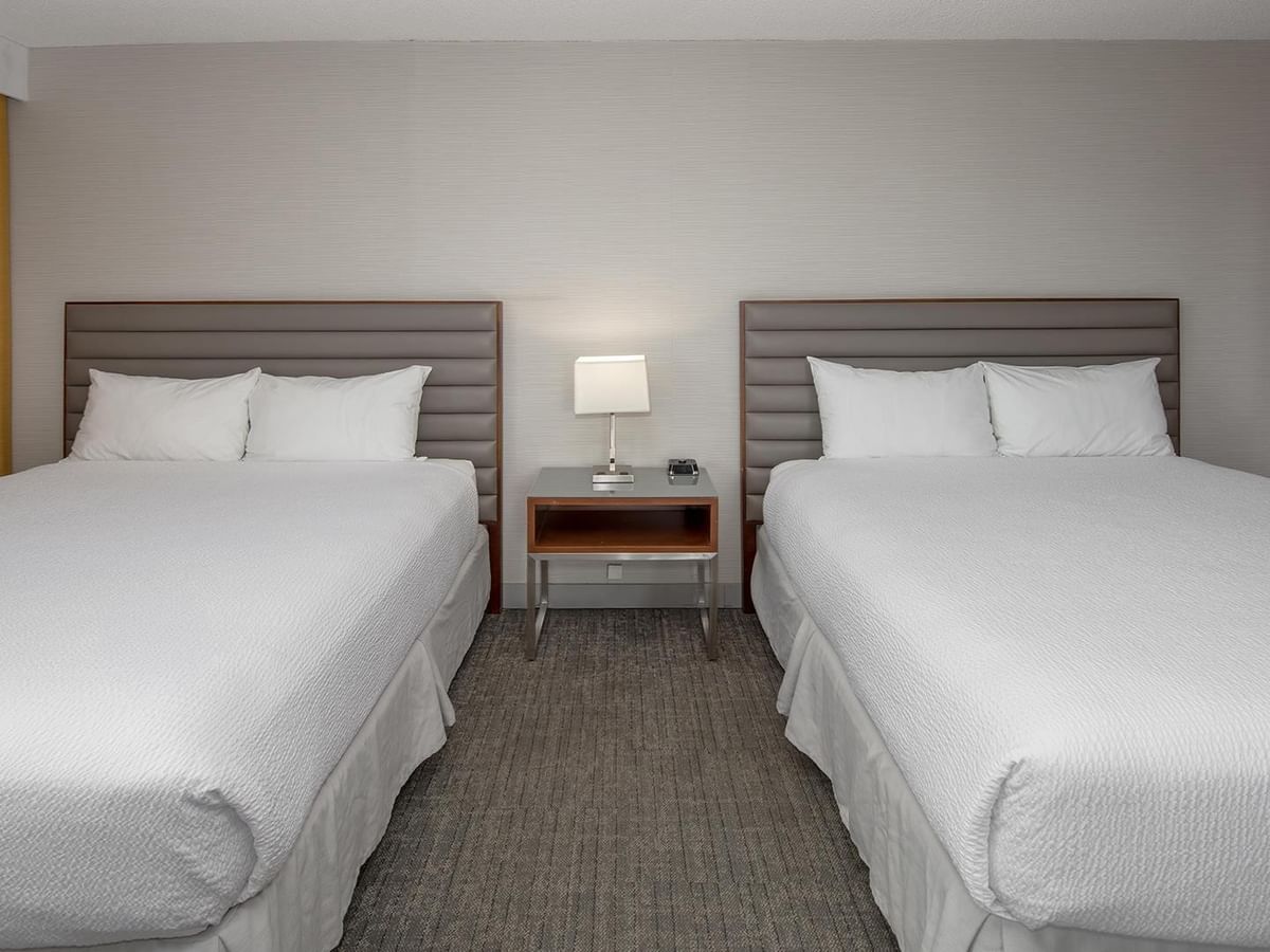 Two queen beds with white linens and upholstered headboards separated by a nightstand at Coast Prince George Hotel.